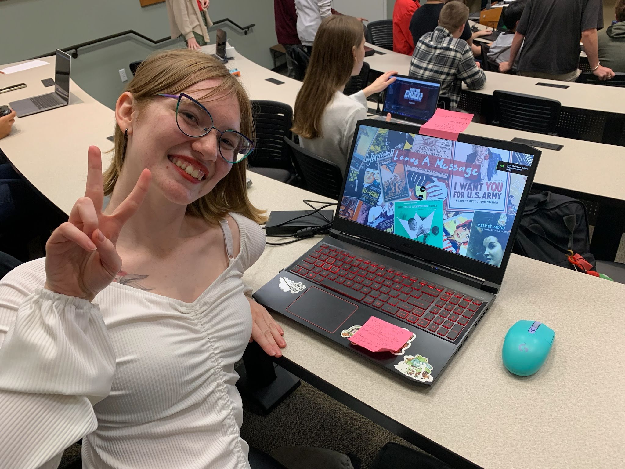 A picture of a strawberry blonde woman posing next to her laptop. The screen shows the video game Leave a Message's main menu.