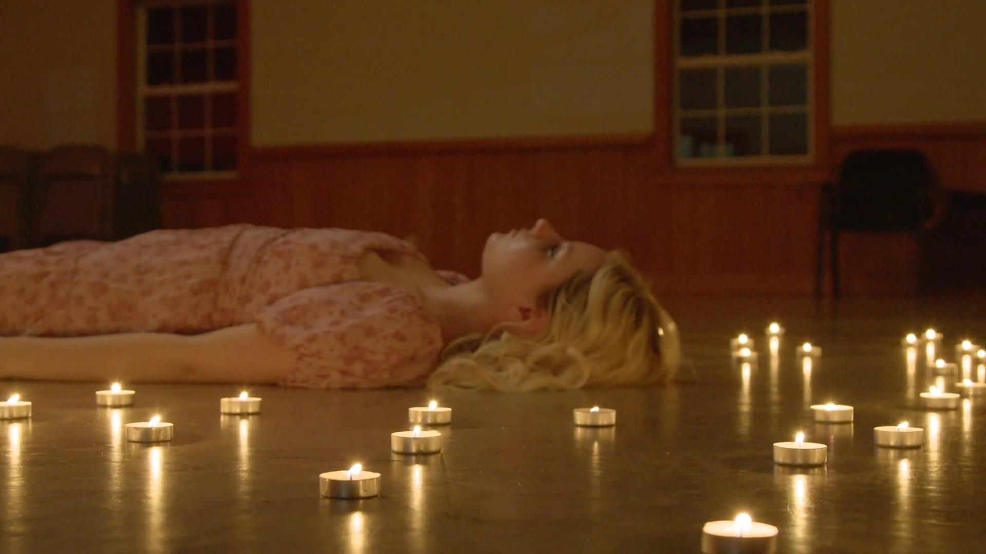 A shot from POWEROUTAGE. A woman diassociates, laying on a cold floor, surrounded by candles.